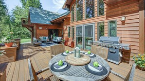 Een houten terras met een ronde tafel, tuinmeubels en een barbecue.