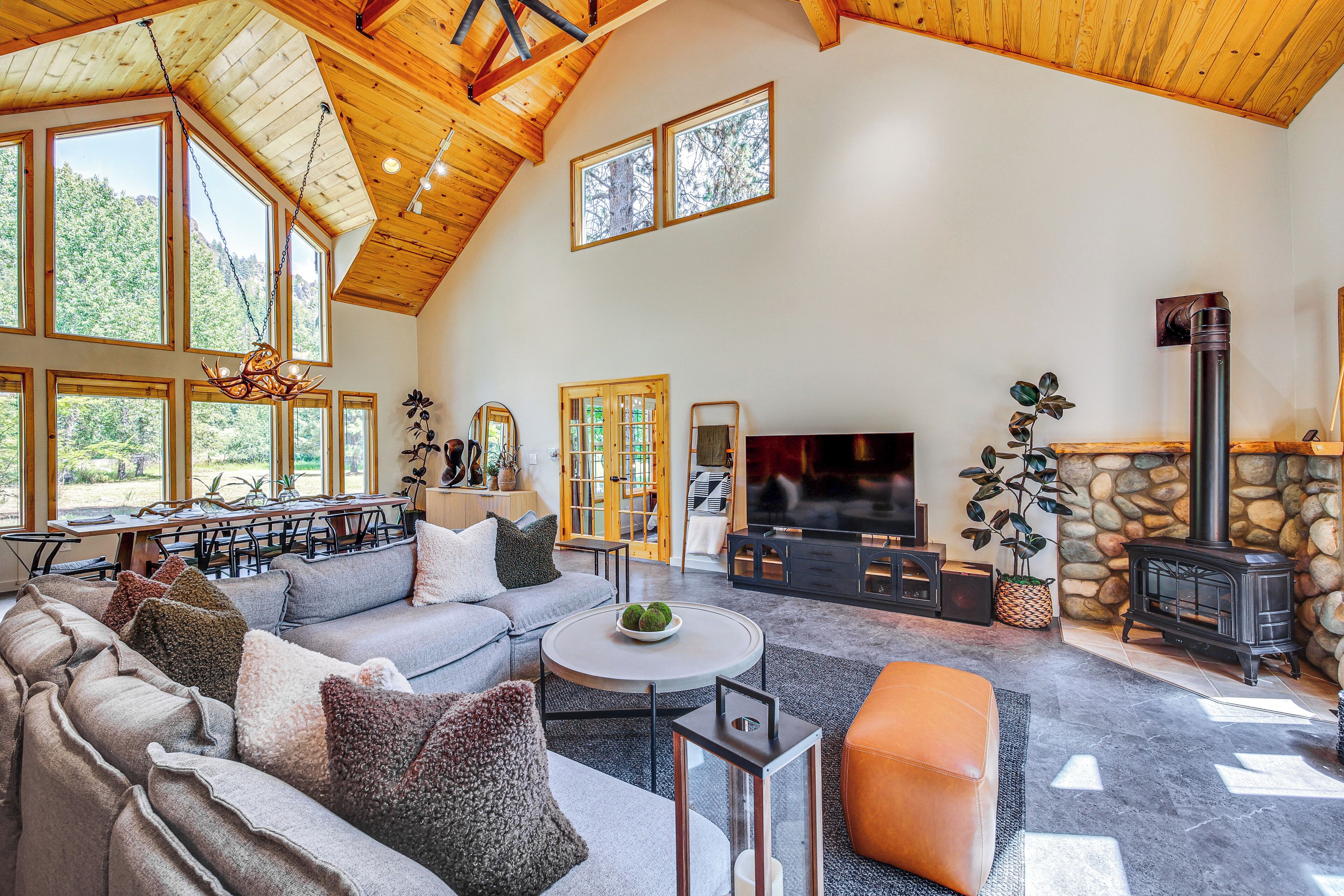 A spacious living room with a high ceiling, large windows, a stone fireplace, and a cozy seating area.