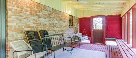 A covered patio with a brick wall, wooden deck, and outdoor seating area with chairs and a bench.