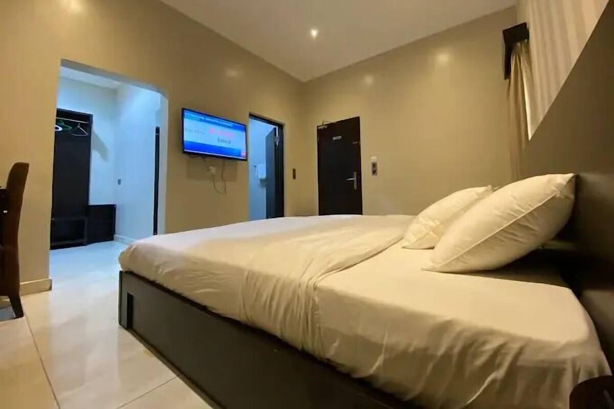 A modern bedroom with a large bed, a flat-screen TV mounted on the wall, and a door leading to a bathroom.