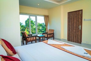 A hotel room with a bed, a small table, two chairs, a window with a view of palm trees, and a wooden door. - Hotel Star Paradise (Port Blair)