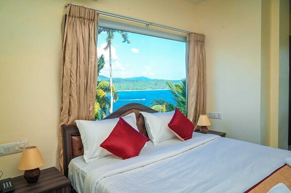 Una habitación de hotel con cama, dos lámparas de noche, una mesita y una ventana con cortinas.