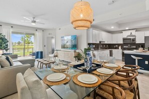 A modern kitchen with white cabinets, a microwave, and a dining area with a glass table set for four.