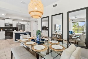 A modern kitchen with white cabinets, a central island, and a dining area with a glass table set for six.