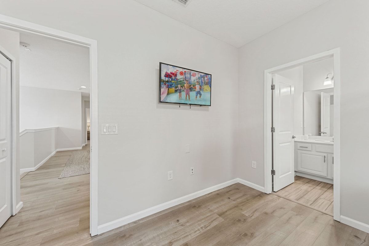 A hallway with a wooden floor, white walls, and a door leading to a bathroom with a mirror.