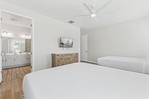 A bedroom with a large bed, a wooden dresser, a ceiling fan, and a wall-mounted TV.