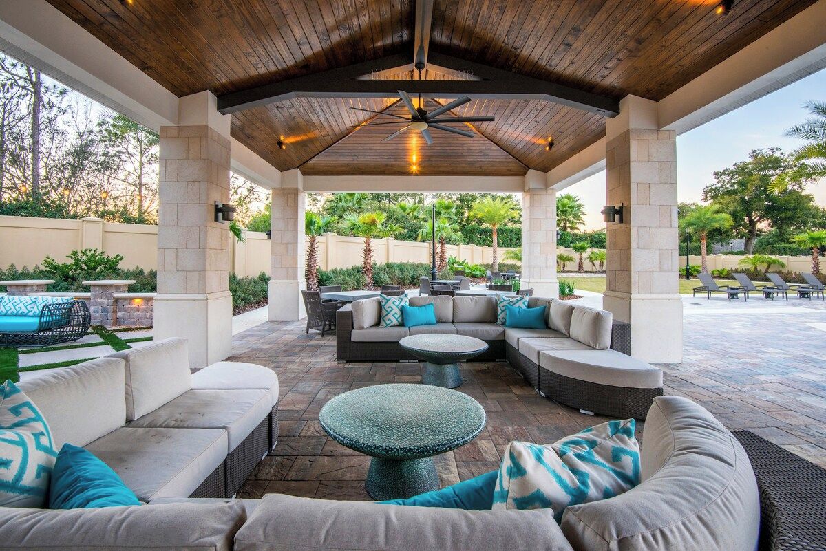 An outdoor patio with a covered seating area, stone flooring, and a ceiling fan.