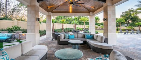 An outdoor patio with a covered seating area, stone flooring, and a ceiling fan.