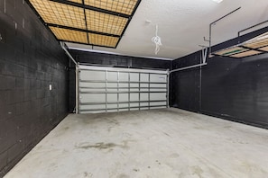 A garage with a metal door, concrete floor, and a ceiling with a grid-like structure. - Stylish Getaway•Pool•Game Room•Near Disney (Kissimmee)