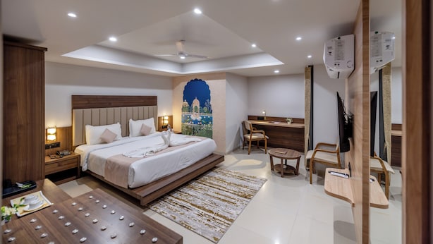 A modern hotel room with a large bed, a desk, a chair, a flat-screen TV, and a ceiling fan. - Hotel Classique, Rajkot (Rajkot)