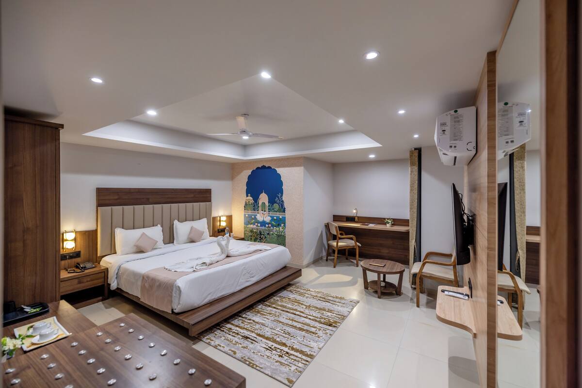 A modern hotel room with a large bed, a desk, a chair, a flat-screen TV, and a ceiling fan.