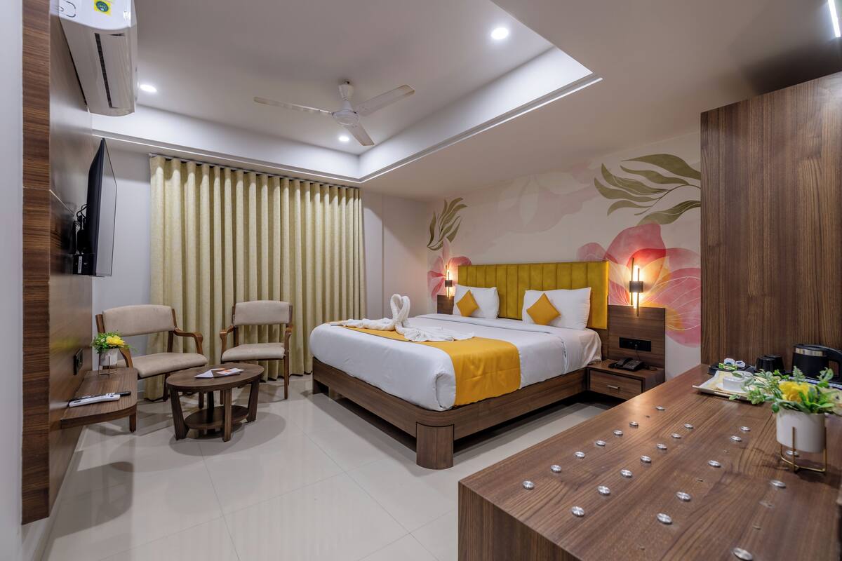 A hotel room with a bed, two chairs, a desk, a nightstand, and a TV.