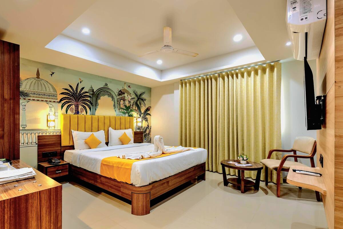 A hotel room with a large bed, a desk, a chair, a small table, and a TV mounted on the wall.