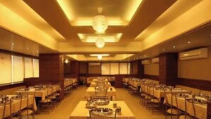 A large banquet hall with multiple round tables and rectangular tables, arranged in rows. - Hotel Classique, Rajkot (Rajkot)