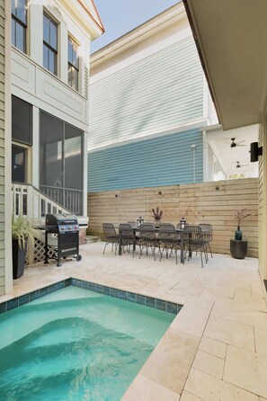 Un jardin avec une piscine, un barbecue et un espace repas comprenant des chaises et une table.