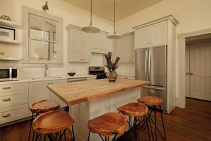 Una cocina moderna con armarios blancos, una isla de madera con taburetes, electrodomésticos de acero inoxidable e iluminación colgante.