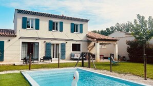 Piscina com flutuador de cisne, um alpendre coberto e uma casa com telhado telhado e persianas.
