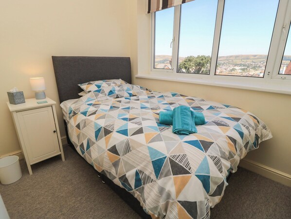 A bedroom with a bed, a nightstand, a lamp, and a window with a view of the countryside. - Purbeck Vista (Swanage)