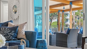 A modern living room with a sofa, a coffee table, and a view of an outdoor balcony area with wicker furniture and a railing.