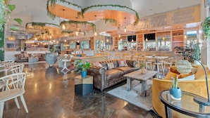 A spacious lobby with a modern design, featuring a leather sofa, wooden chairs, and a bar area in the background.