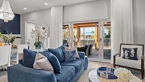 A modern living room with a blue sofa, white curtains, and a view of an outdoor pool area.