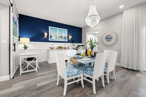 A modern dining area with a blue accent wall, white furniture, and a chandelier.