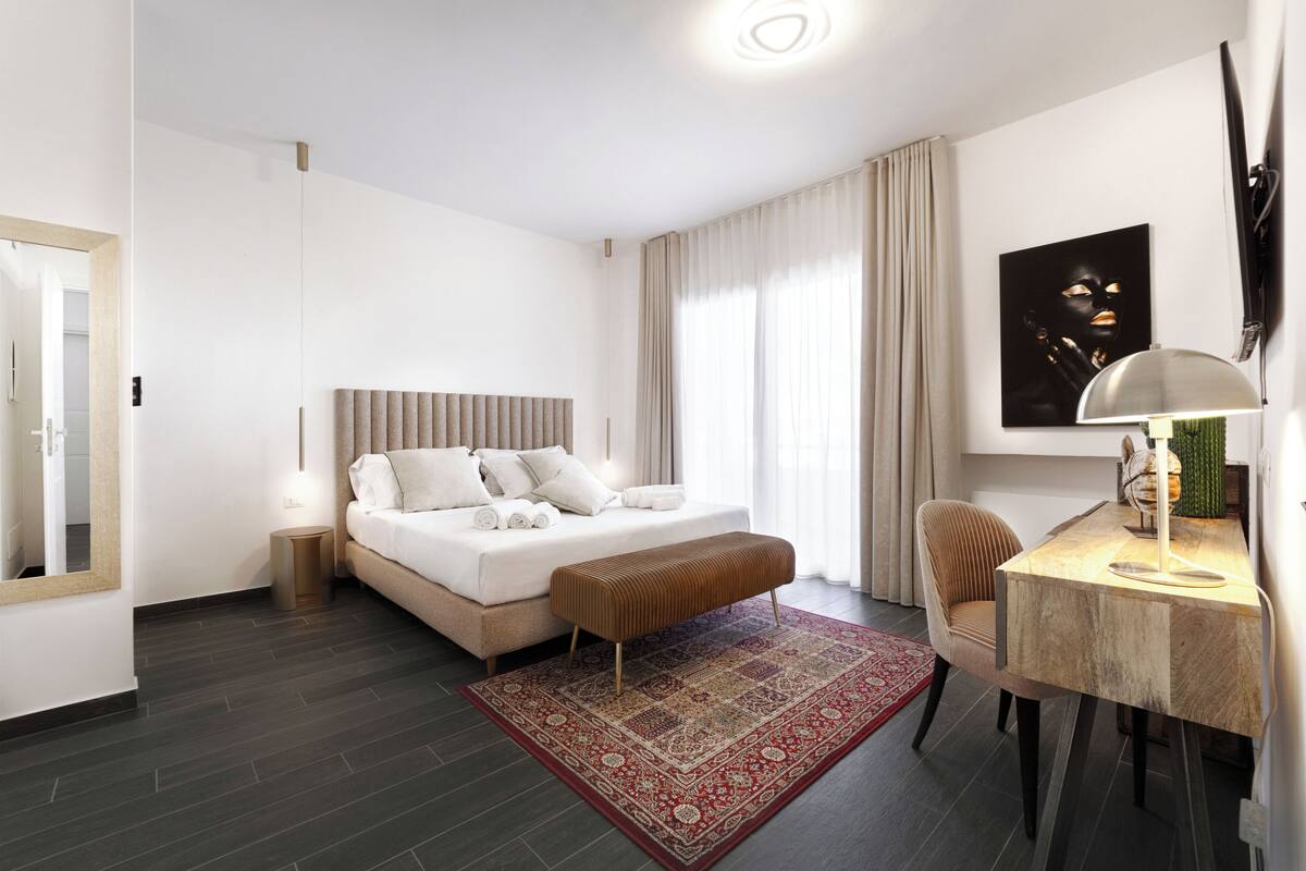 Una camera d'albergo moderna con un letto grande, una scrivania con una lampada e un tappeto rosso decorato.