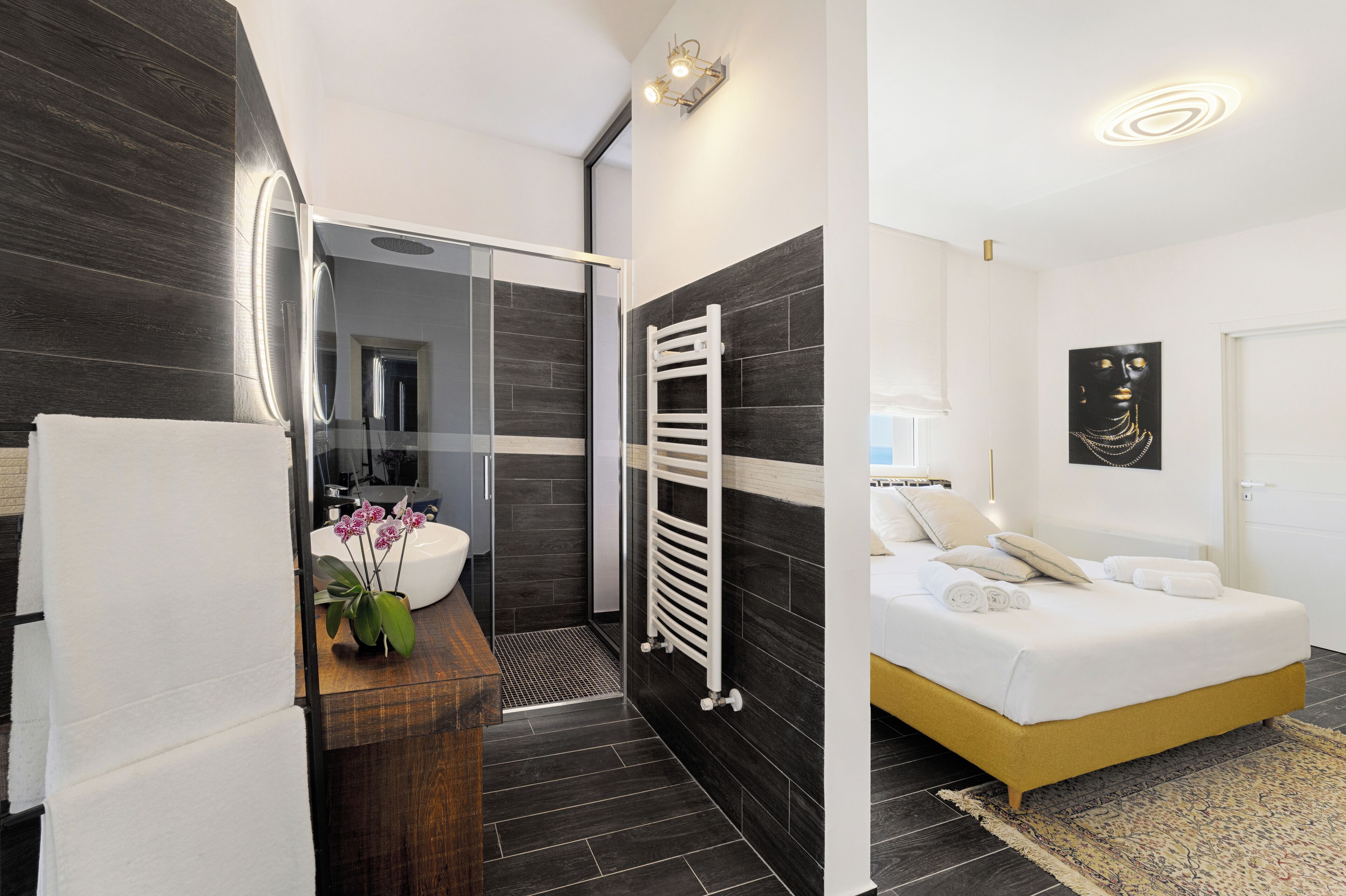 Un bagno moderno con box doccia in vetro, un porta asciugamani bianco e un lavabo con un vaso di fiori.