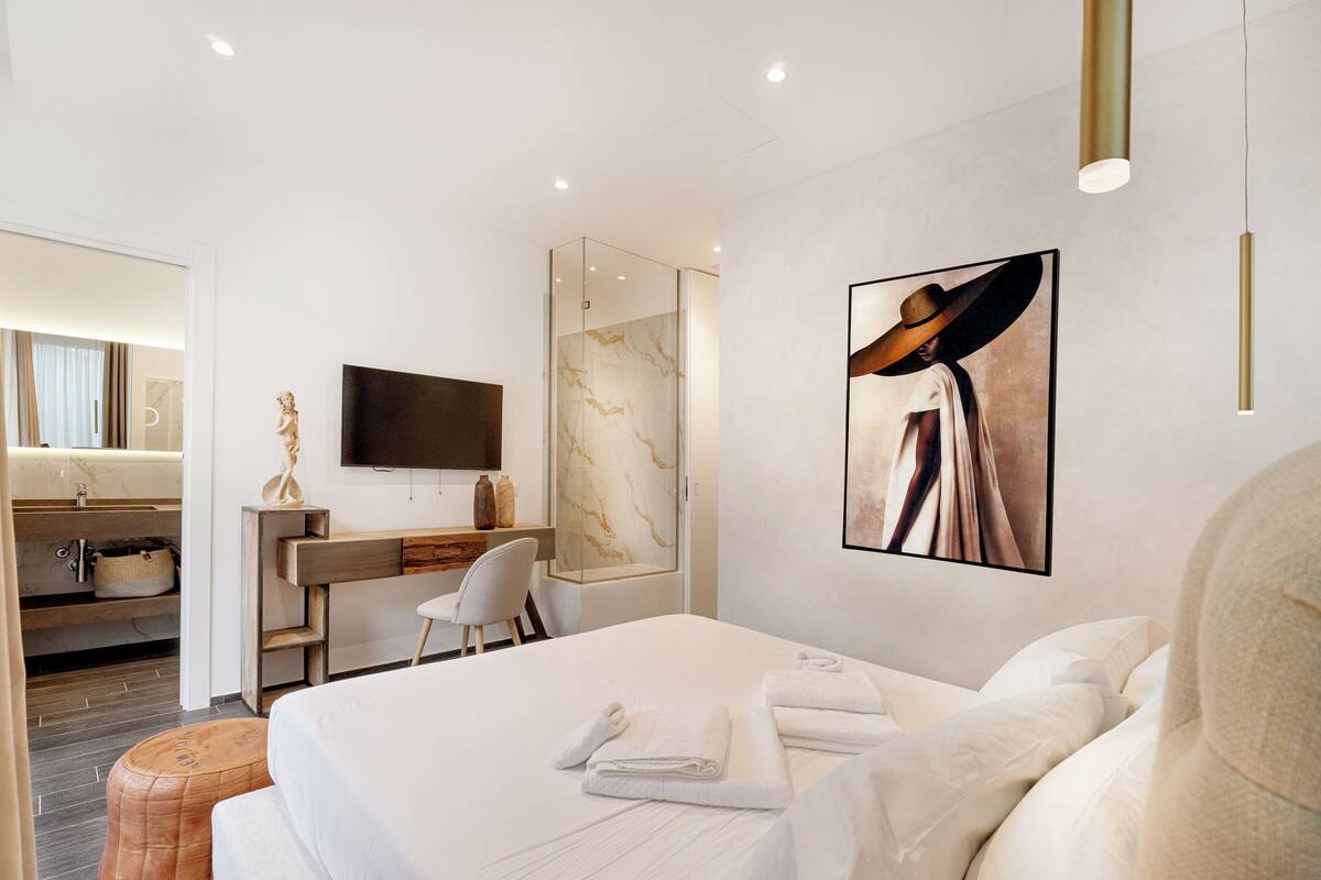 Una moderna camera d'albergo con un letto, una scrivania, una sedia, una TV e un quadro di grandi dimensioni appeso al muro.