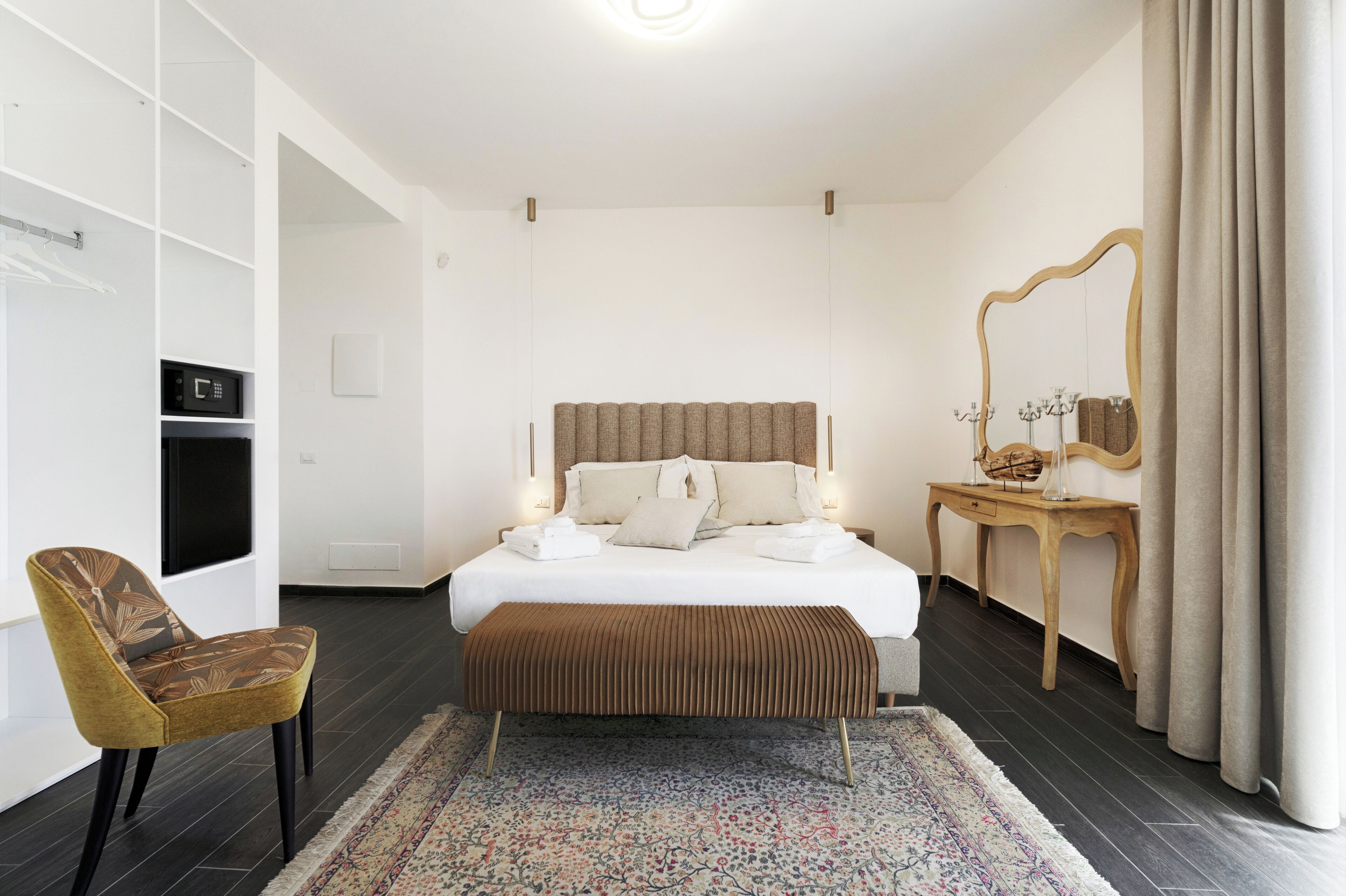 Una habitación de hotel moderna con una cama grande, una mesita de noche de madera, una silla, un espejo y un televisor integrado.