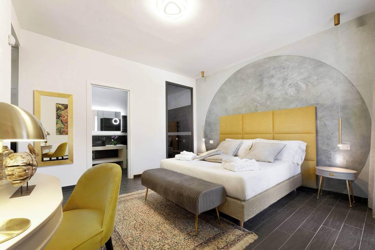 Camera da letto moderna con un letto grande, una poltrona gialla, un tavolino rotondo e un arco originale sulla parete.