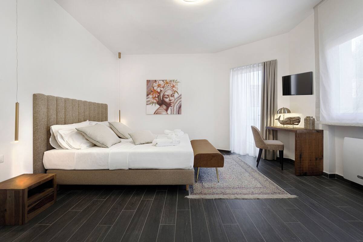 Una camera da letto moderna con un letto, un comodino, una scrivania, una sedia e un'opera d'arte appesa al muro.