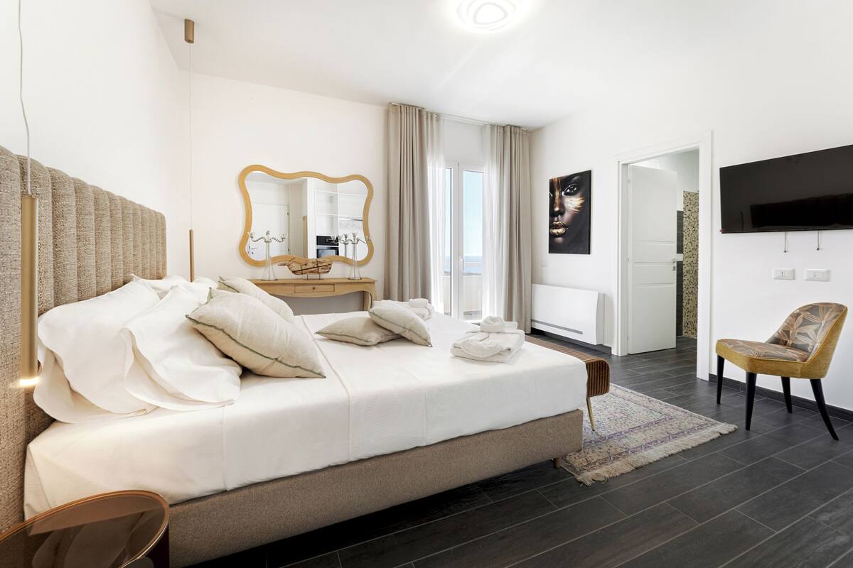 Una camera d'albergo moderna con un letto grande, un comò con uno specchio, una TV a schermo piatto e vista sulla città.