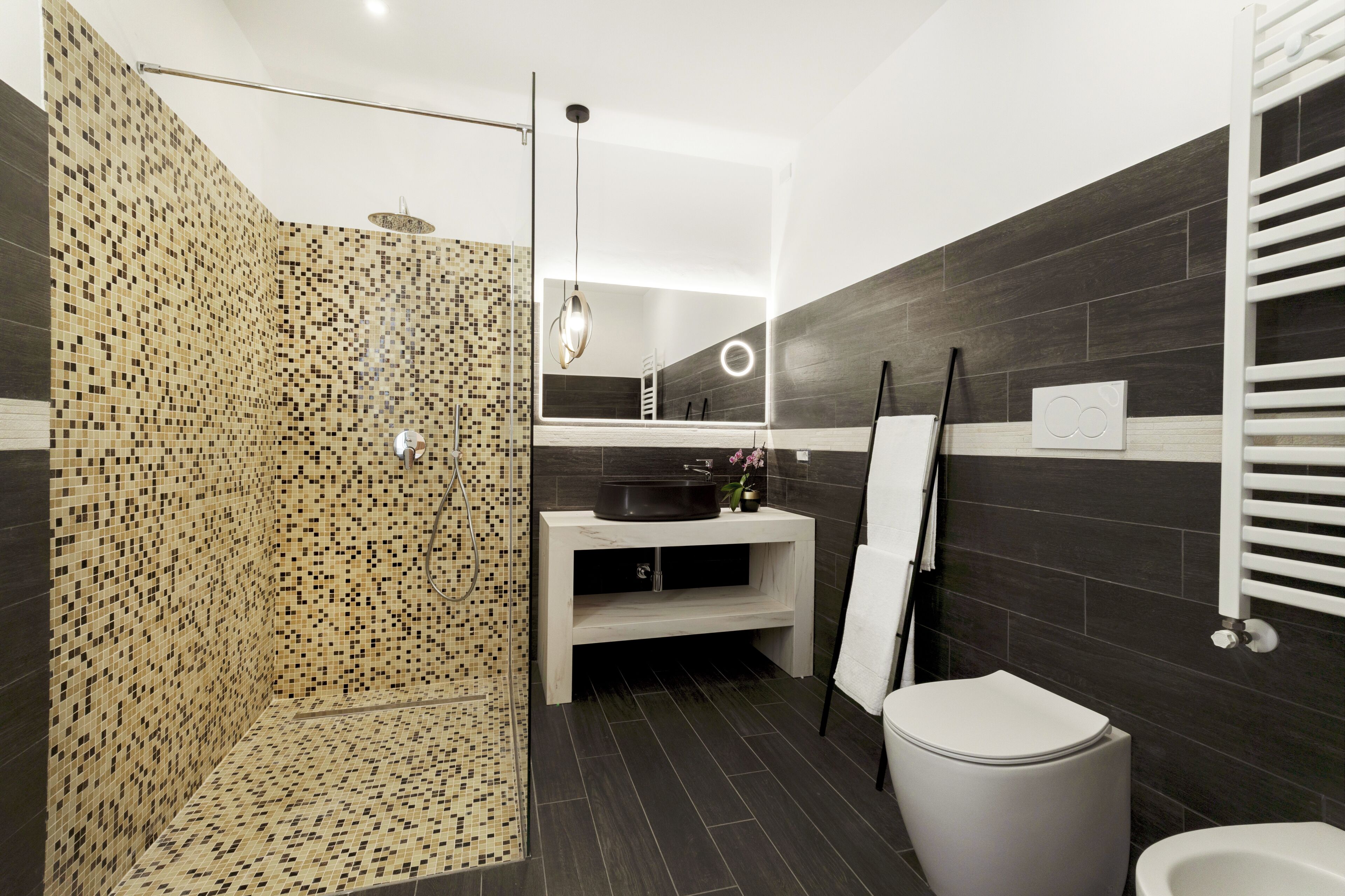 Een moderne badkamer met een mozaïekdouche, een witte wastafel, een toilet en een handdoekrek.