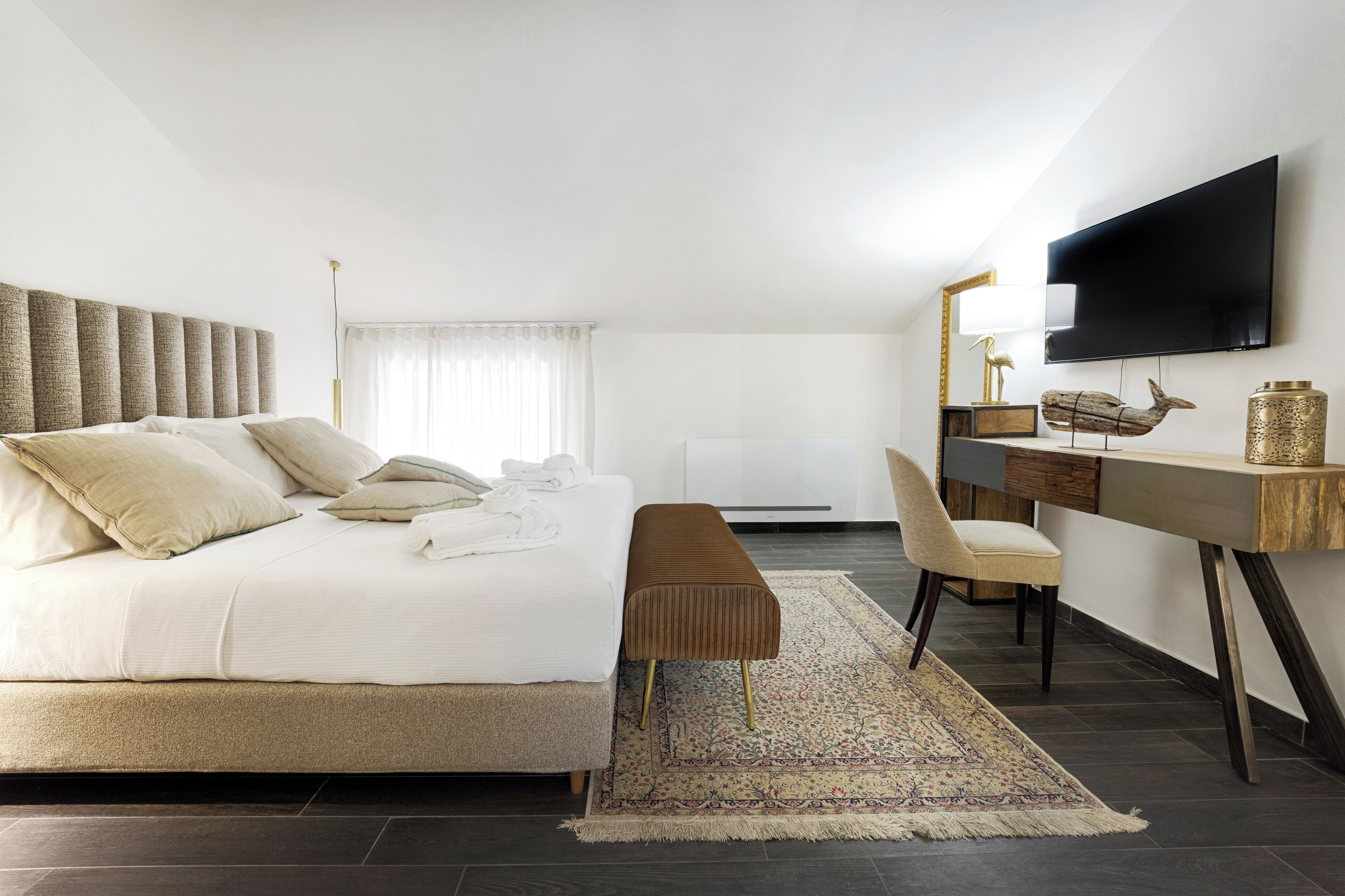 A modern bedroom with a large bed, a desk, a chair, and a TV.