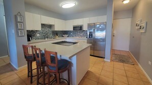 Una cocina moderna con una isla central, taburetes de bar, un refrigerador de acero inoxidable y un protector contra salpicaduras de piedra.