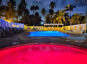 A swimming pool with a red and blue color scheme, surrounded by palm trees and a building with a white facade. - 3-bedroom condo in superb Isabela with WiFi, fitness room, AC (Isabela)