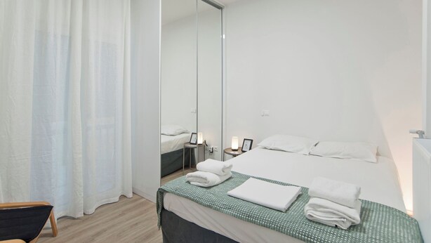 A hotel room with a large bed, a mirror, a bedside table with a lamp, and a chair. - Aether Athens Luxurious Fully Renovated Apt (Athina)