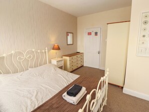 A bedroom with a bed, a dresser, a nightstand, a lamp, and a door with a sign. - 2 The Crescent (Seascale)