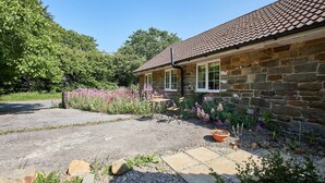 A stone house with a tiled roof, a gravel driveway, and a garden with flowering plants. - Host & Stay | Lane Farm Cottage (Easington)