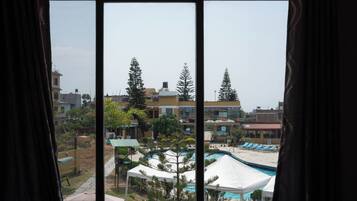 Vista a través de una ventana de un hotel con piscina, sillones de descanso y una carpa.