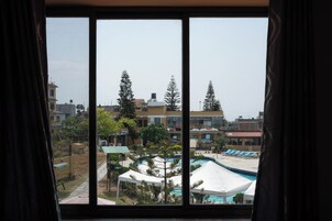 Vista a través de una ventana de un hotel con piscina, sillones de descanso y una carpa.