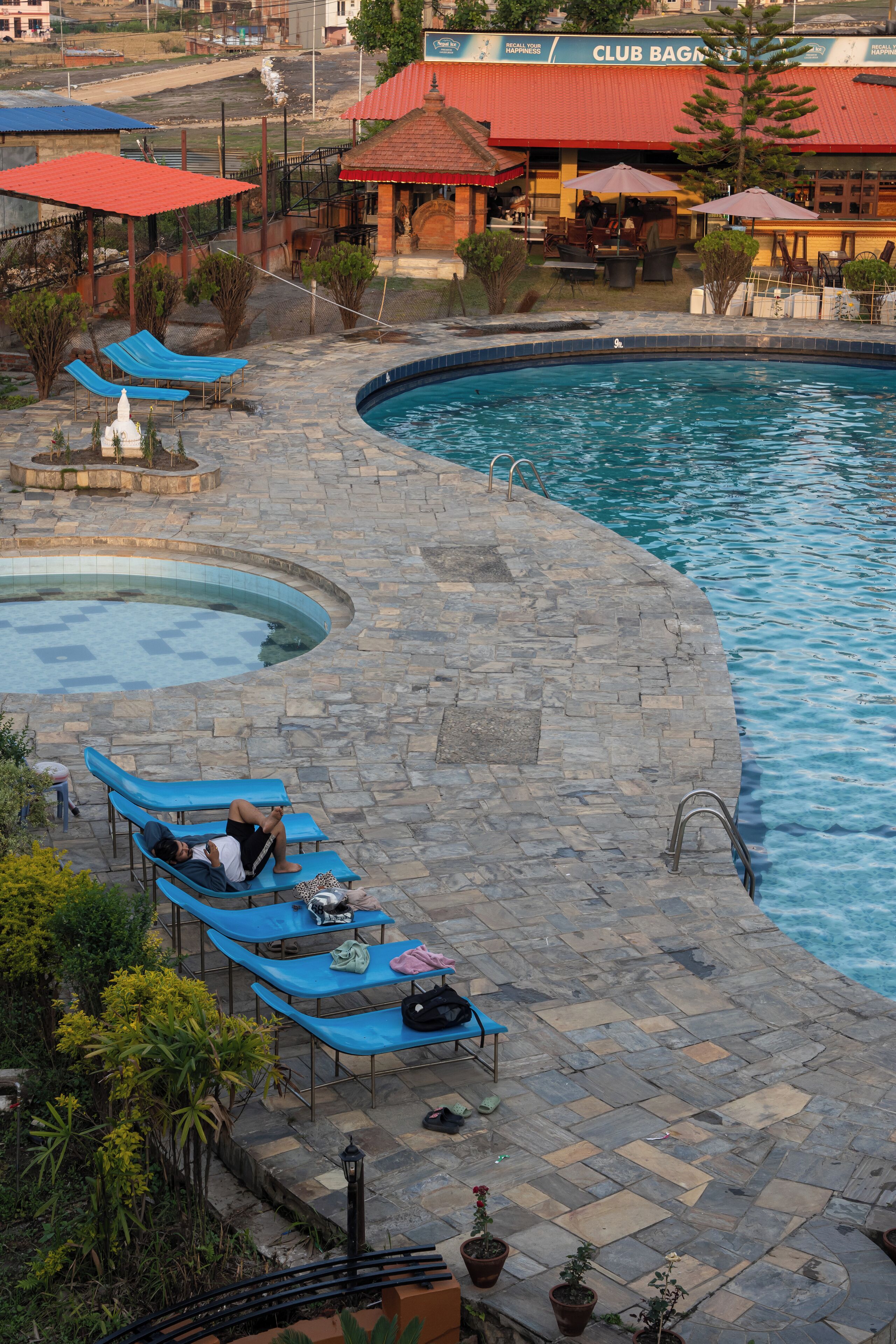 A pool area with blue lounge chairs, a stone deck, and a Club Bagel building in the background.