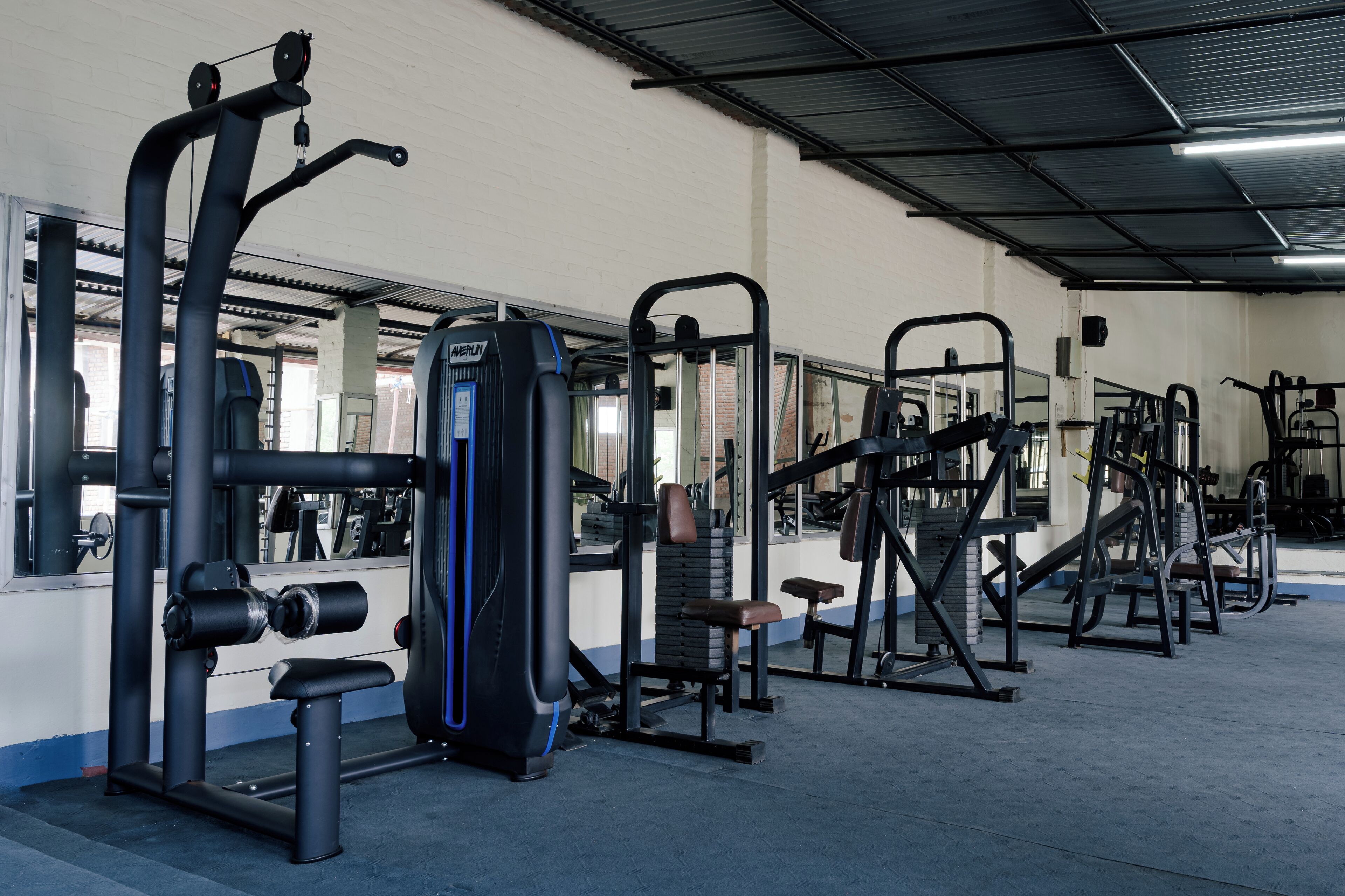 A gym with various exercise machines, mirrors, and a bench.