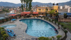 A swimming pool with lounge chairs and a restaurant in the background. - Club Bagmati by HSH (Suryabinayak)