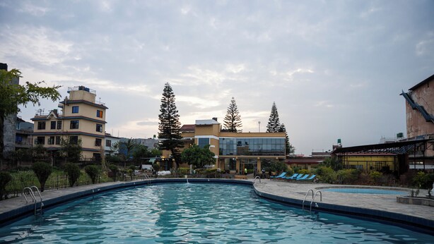 A swimming pool with a view of surrounding buildings and trees. - Club Bagmati by HSH (Suryabinayak)