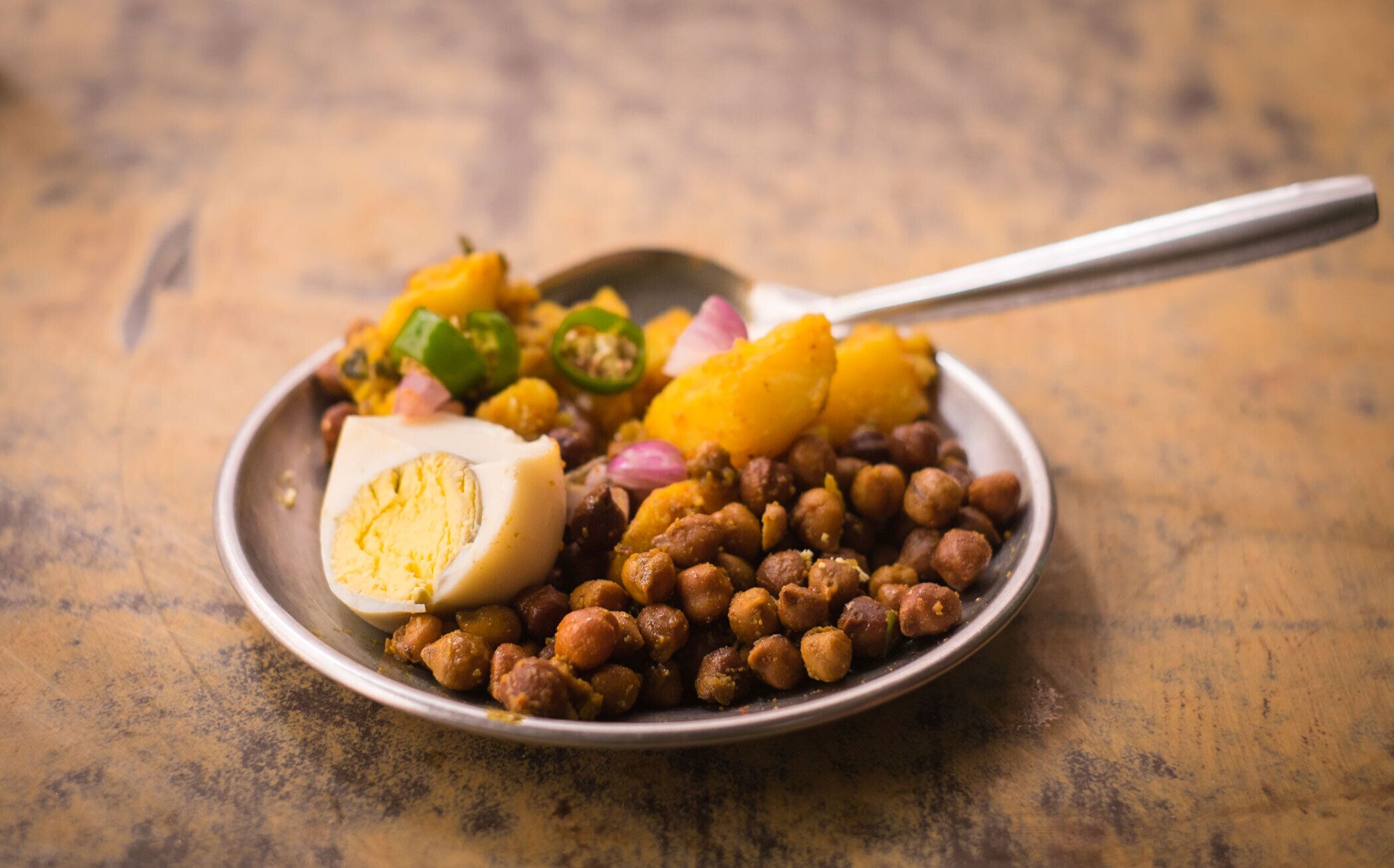 A bowl of food with chickpeas, a halved boiled egg, diced red onions, and yellow squash.