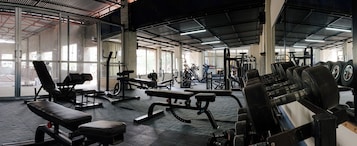 Un gimnasio con diversos equipos de ejercicio, ventanas amplias y un techo alto.