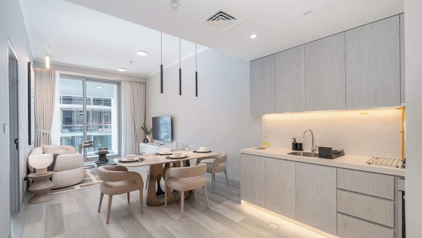 A modern kitchen with a built-in oven, a sink, and a dining area with a table and chairs. - StayShort - Amazing 1 Bedroom in Concept 7 JVC Sleeps 2 (Jumeirah Village Circle)