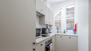 Une cuisine avec des meubles blancs, un four à micro-ondes, un grille-pain et une fenêtre donnant sur la rue.